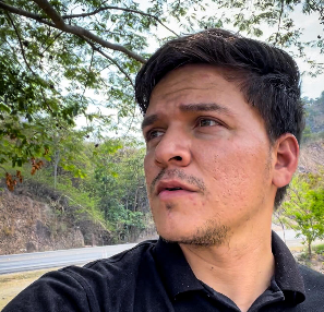 Retrato de un hombre mirando hacia la distancia al borde de una carretera en una zona montañosa de Honduras.