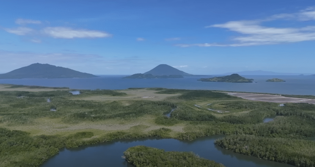 Vista aérea de islas verdes y manglares en el Golfo de Fonseca, con montañas y cielo azul al fondo.
