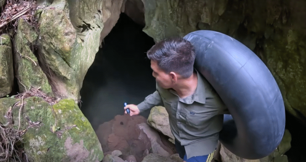 Hombre con camiseta verde descendiendo a una cueva con un neumático inflable en el brazo durante una aventura de espeleología en Olancho.