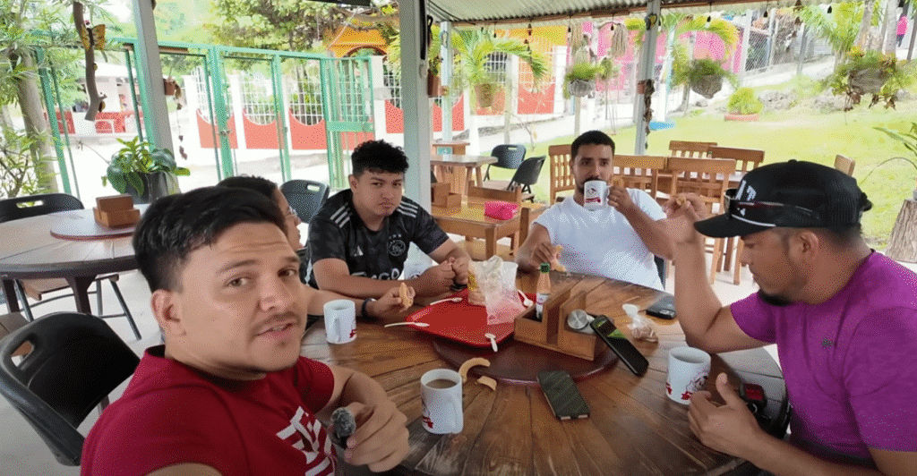 Grupo de cuatro hombres disfrutando de café y comida alrededor de una mesa en un restaurante al aire libre en Francisco Morazán; uno de ellos mira a la cámara.