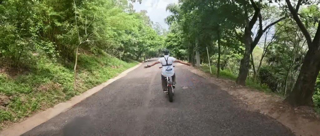 Motorista con casco conduce una motocicleta en una carretera bordeada de frondosos árboles verdes en Francisco Morazán, visto desde atrás durante el día.