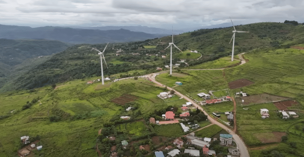Vista aérea de colinas verdes en Francisco Morazán con aerogeneradores blancos, casas dispersas y caminos serpenteantes bajo un cielo nublado.