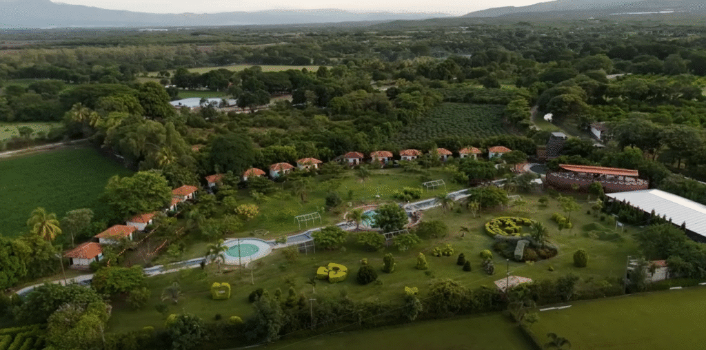 Vista aérea de un complejo turístico en Comayagua, con cabañas de techo rojo alineadas en hilera, piscina circular, áreas verdes y campos agrícolas alrededor, con montañas al fondo.