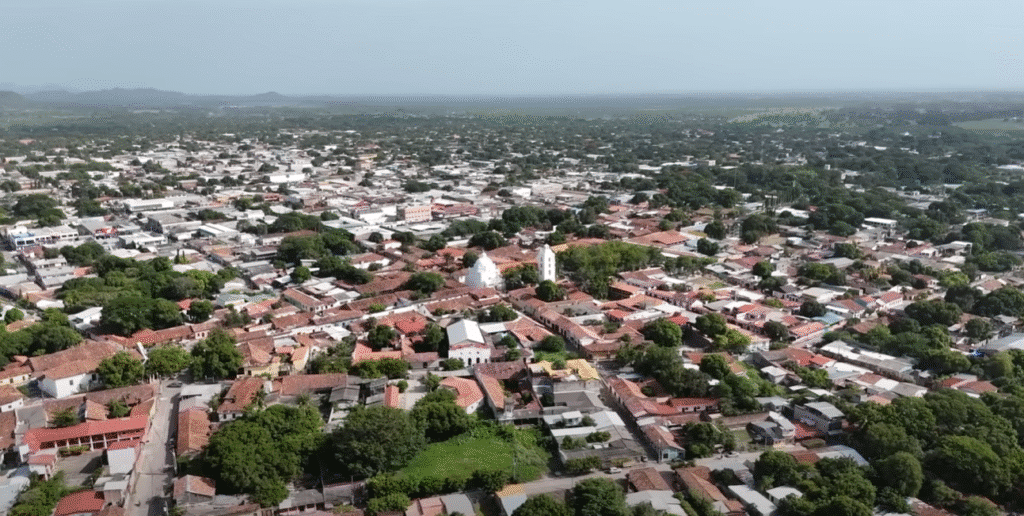 Vista aerea de la ciudad de Choluteca con casas de techo de tejas rojas, arboles y un campanario blanco al fondo.