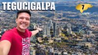 Un hombre sonriente se toma una selfie con la panorámica de la ciudad de Tegucigalpa y un gráfico con el número 7.