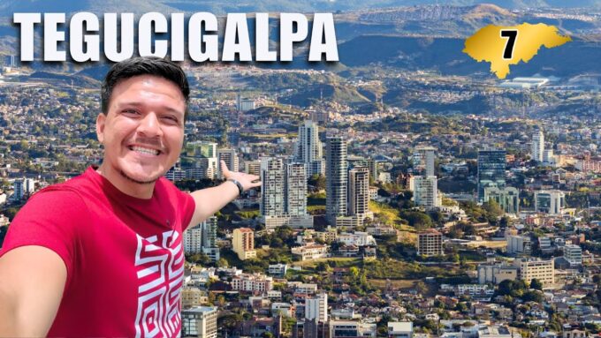 Un hombre sonriente se toma una selfie con la panorámica de la ciudad de Tegucigalpa y un gráfico con el número 7.