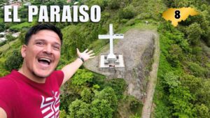 Un hombre sonriente se toma una selfie frente a una cruz blanca en la cima de un cerro verde en El Paraíso, Honduras.