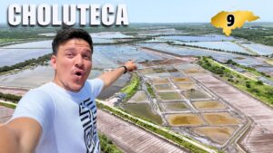 Un hombre se toma una selfie frente a las salinas de Choluteca con un rótulo que dice Choluteca y un marcador amarillo con el número 9.