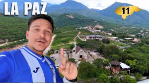 Un hombre con camiseta de fútbol de Honduras posando frente a un pueblo en un valle verde en La Paz, Honduras.